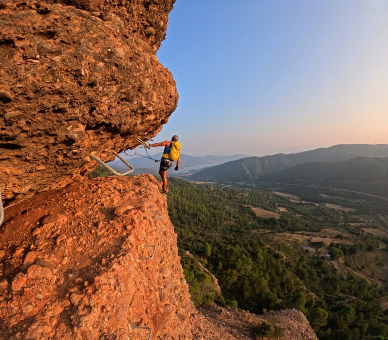 Una persona realitzant un pas horitzontal per les grapes de la via ferrada Roca Foradada amb vistes al pantà de Sant Antoni i la Pobla de Segur.