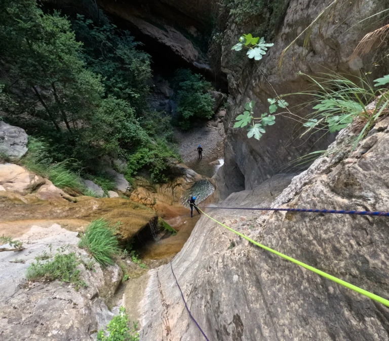 Un noi baixant en ràpel per una paret de roca vertical i estreta a l'engorjat del barranc de Gurp.