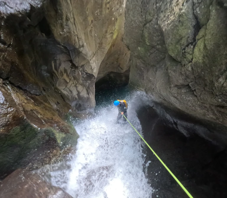 Una persona fent un ràpel per una gran cascada d'aigua en un entorn d'alta muntanya al barranc de Núria.