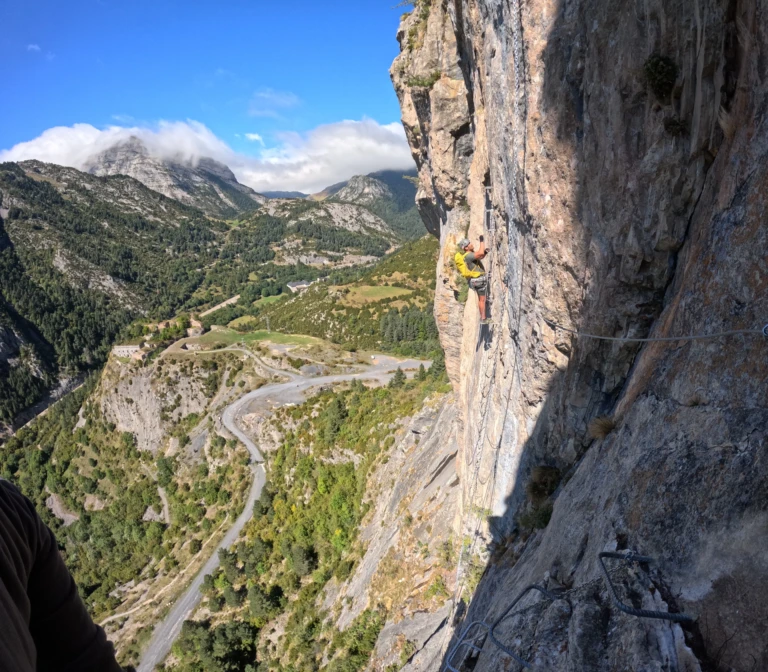 Un noi progressant per les grapes de ferro en una paret vertical de la via ferrada Roca Narieda amb vistes a la vall de l'Alt Urgell.