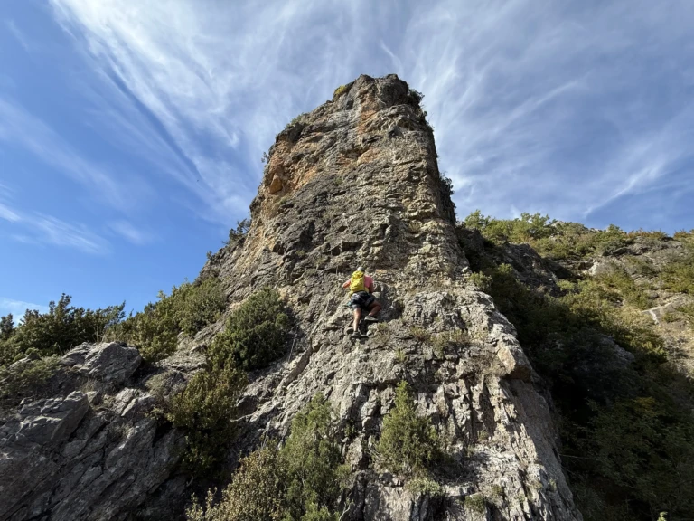 Una persona pujant per una paret de roca equipada amb esglaons de ferro i cable de seguretat a la via ferrada Tossal de Miravet.