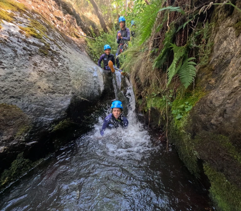 un nen lliscant junts per un tobogan natural d'aigua en un barranc assolellat.