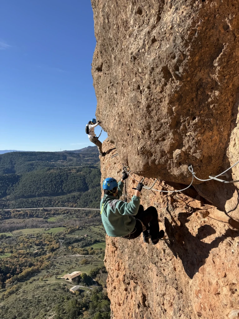 Un noi i una noia progressant per un tram extraplomat de la via ferrada, subjectant-se als esglaons amb força i tècnica.