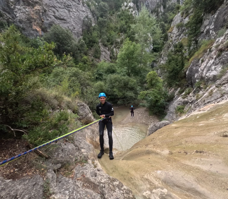 Un jove fent un ràpel per una paret de roca calcària amb una cascada d'aigua cristal·lina al barranc de Bóixols.