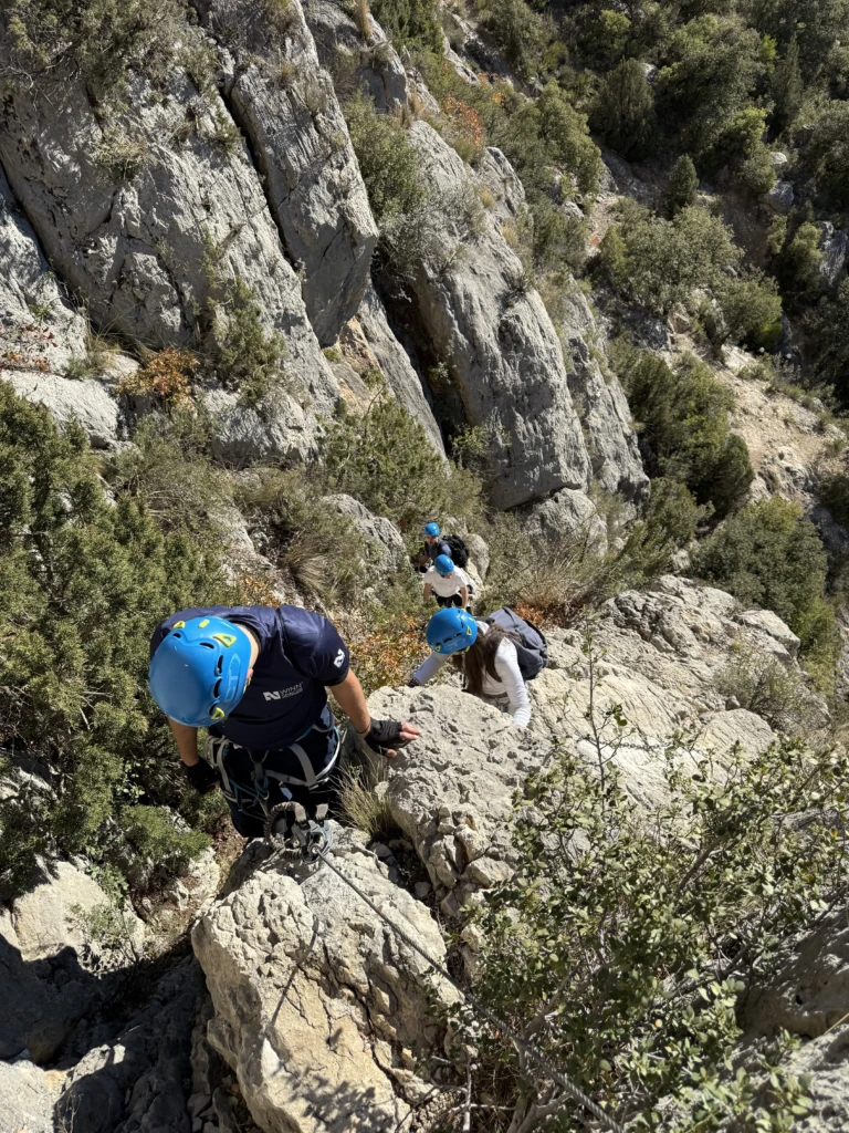 Un grup de joves equipats amb cascs i arnesos pujant en fila per la paret equipada de la via ferrada Teletubbies a Lleida.